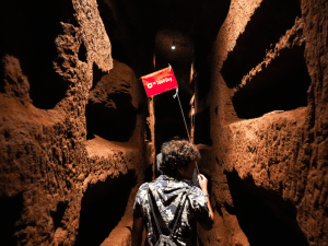 Man walking in catacombs holding a Tour Guy flag.