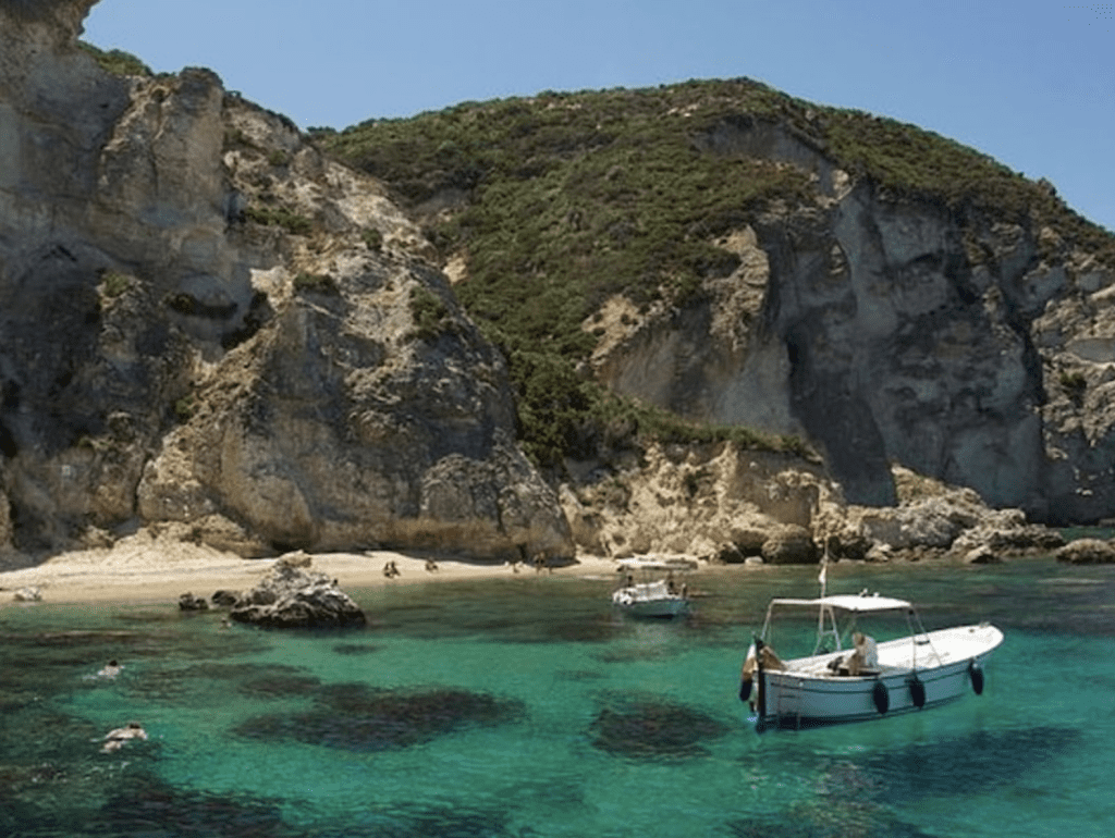 A small boat sits on crystal clear blue-green water in Italy.