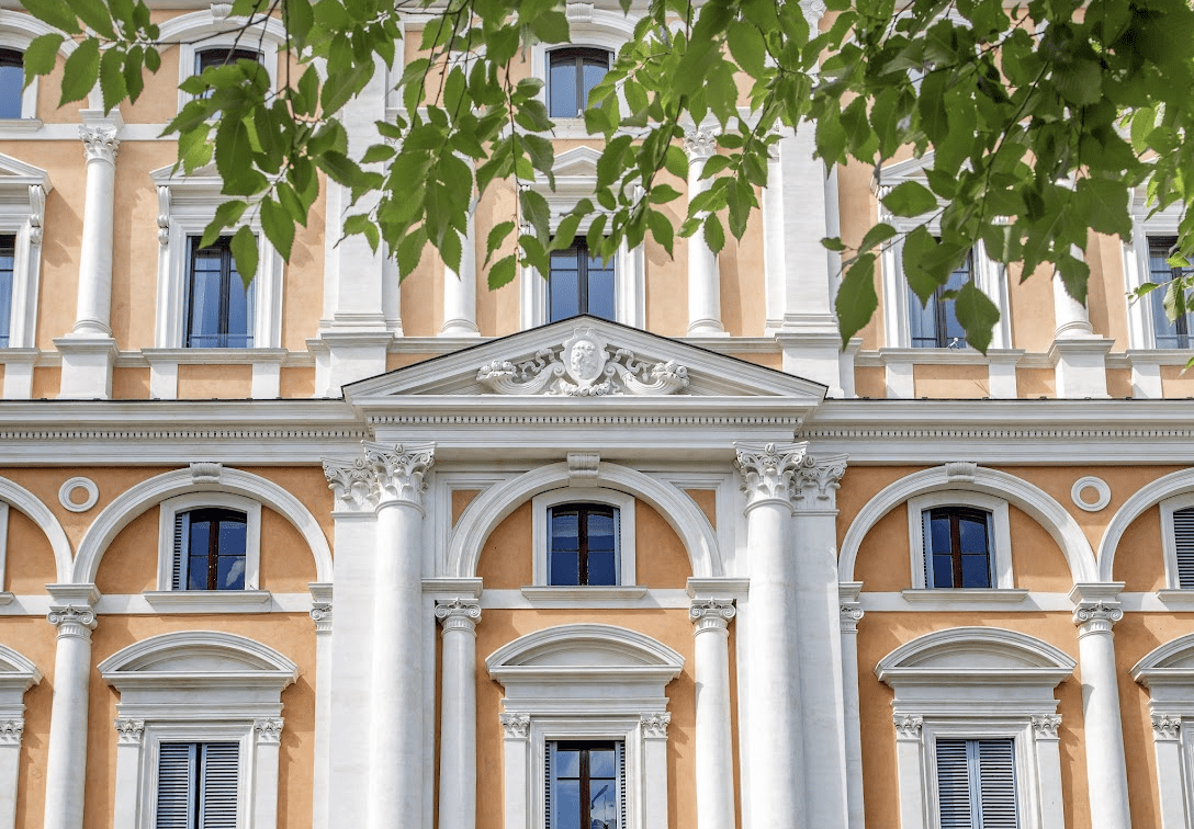 White and cream pillared stone building with trees out front.