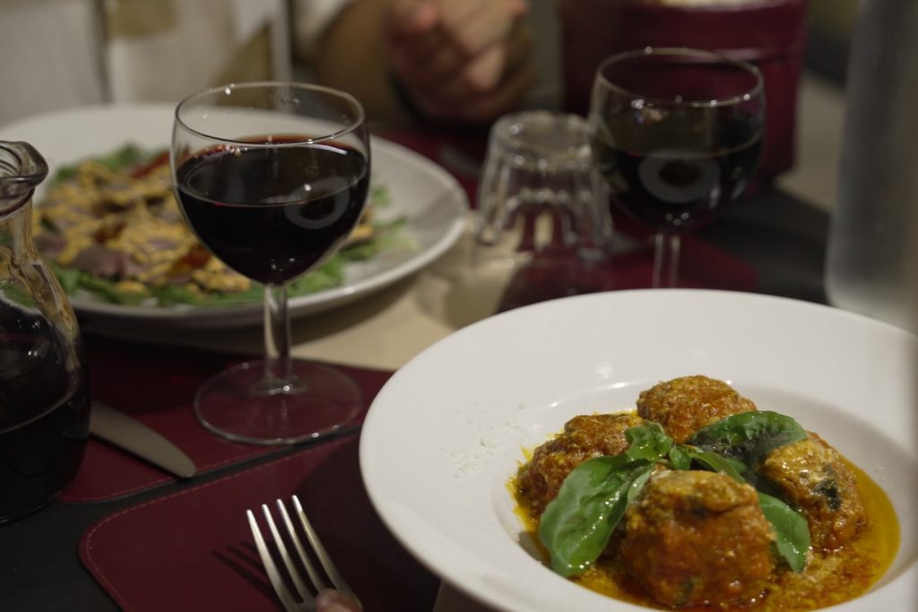 A glass of wine and a plate of meatballs. 