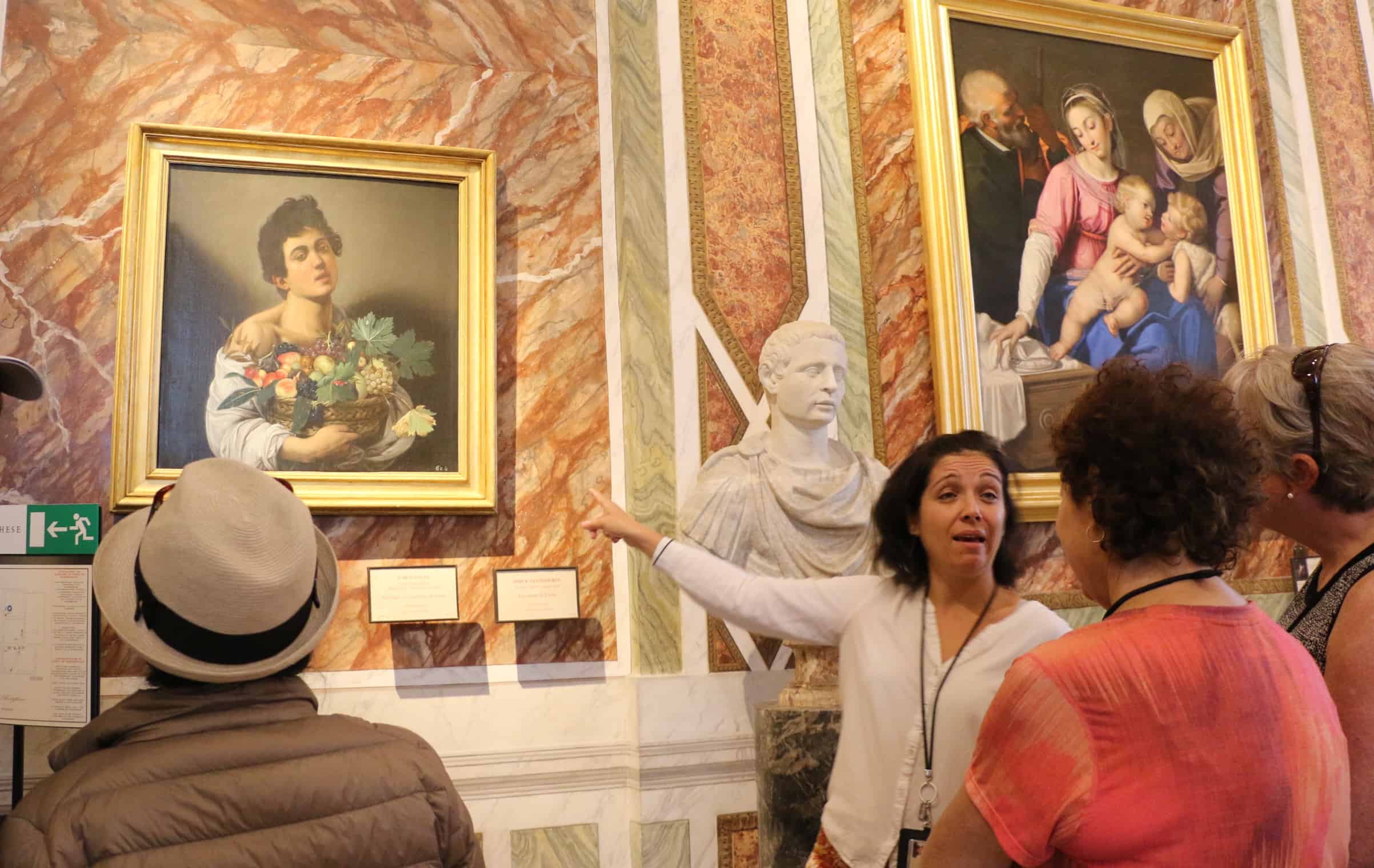 Tour guide showing the Boy with Basket of Fruit painting by Caravaggio to a group of visitors in the Borghese Gallery in Rome.