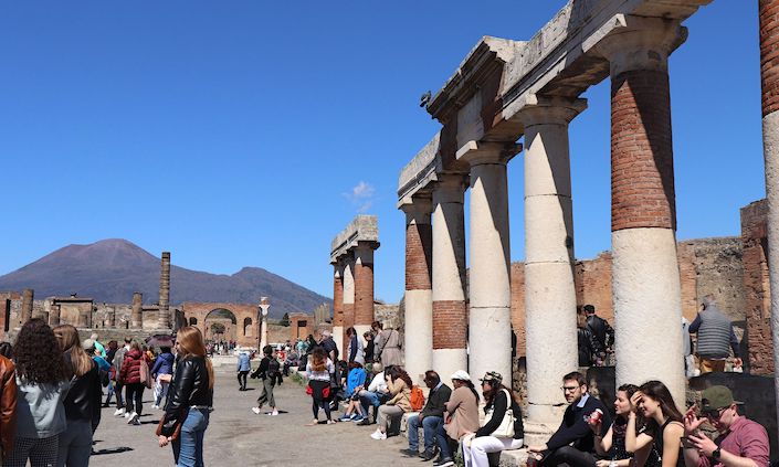 Visitors walking around the structures in the Pompeii archeological park with Mt. Vesuvius in the background.