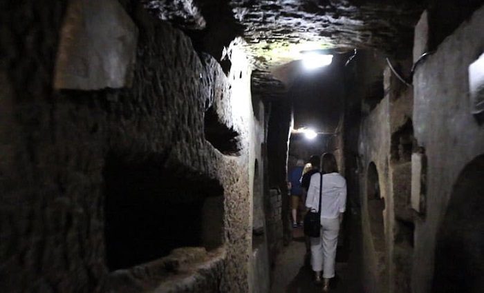 A woman walking through the dark narrow tunnel of the catacombs in Rome