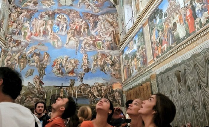 People looking up at the ceiling in the Sistine Chapel with Michelangelo's The Last Judgement in the background.
