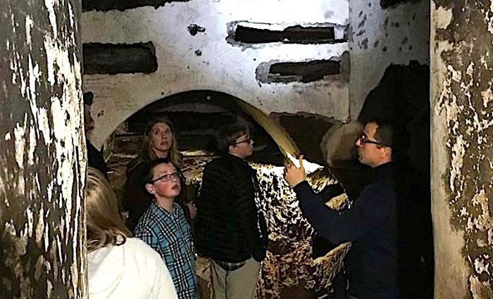 People on a guided tour walking through the underground tunnels of the catacombs in Rome